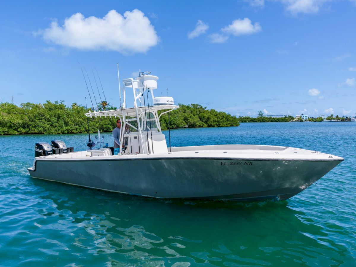 A sleek white fishing/ sport boat floats on turquoise water near a green mangrove shoreline under a blue sky, with clear, sunny weather.