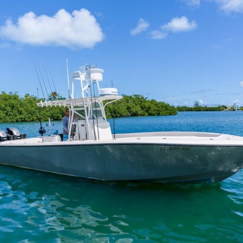 A sleek white sportfishing boat on clear turquoise waters near a green mangrove shoreline under a sunny blue sky.
