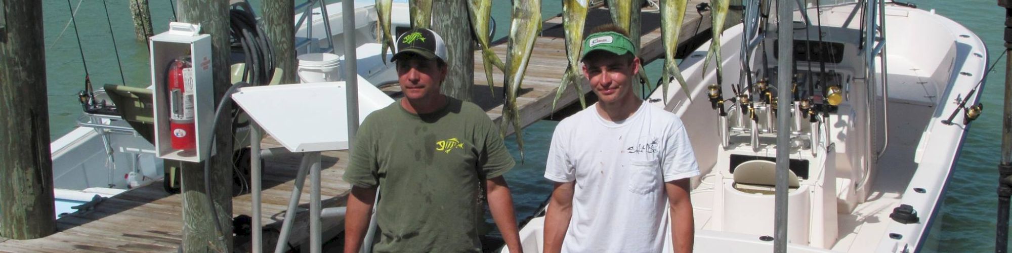 Two men stand behind a display of freshly caught fish on a dock, with a &ldquo;RUN & GUN&rdquo; sign in the background.