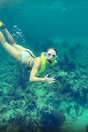 A person snorkeling underwater, wearing a life vest and fins, gliding over a coral reef with clear blue water around them.