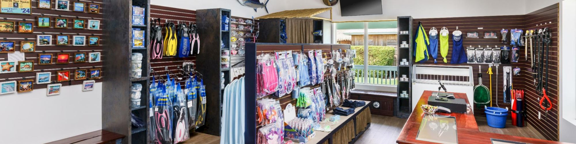 A bright store with outdoor gear and clothing on racks, shelves full of apparel, a glass counter, and a mounted fish on the wall.